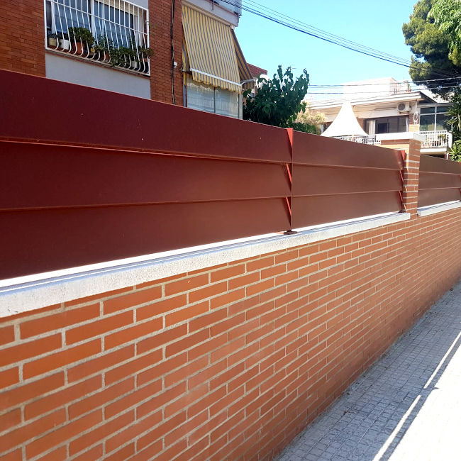 Imatge d'una reixa de xapa de ferro pintada en vermell pel mur d'entrada a un bloc de pissos
